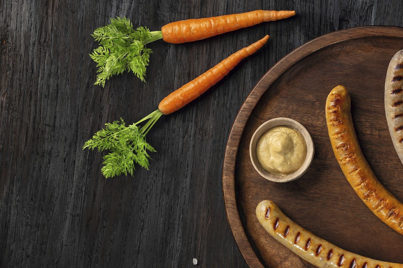 Drei hybride Bratwurstvarianten – mit Karotte, Mais und Rotkohl – auf einem Brett vor dunklem Hintergrund. Beispiel für moderne Hybridprodukte für Metzgereien, Lebensmittelindustrie und Systemgastronomie.