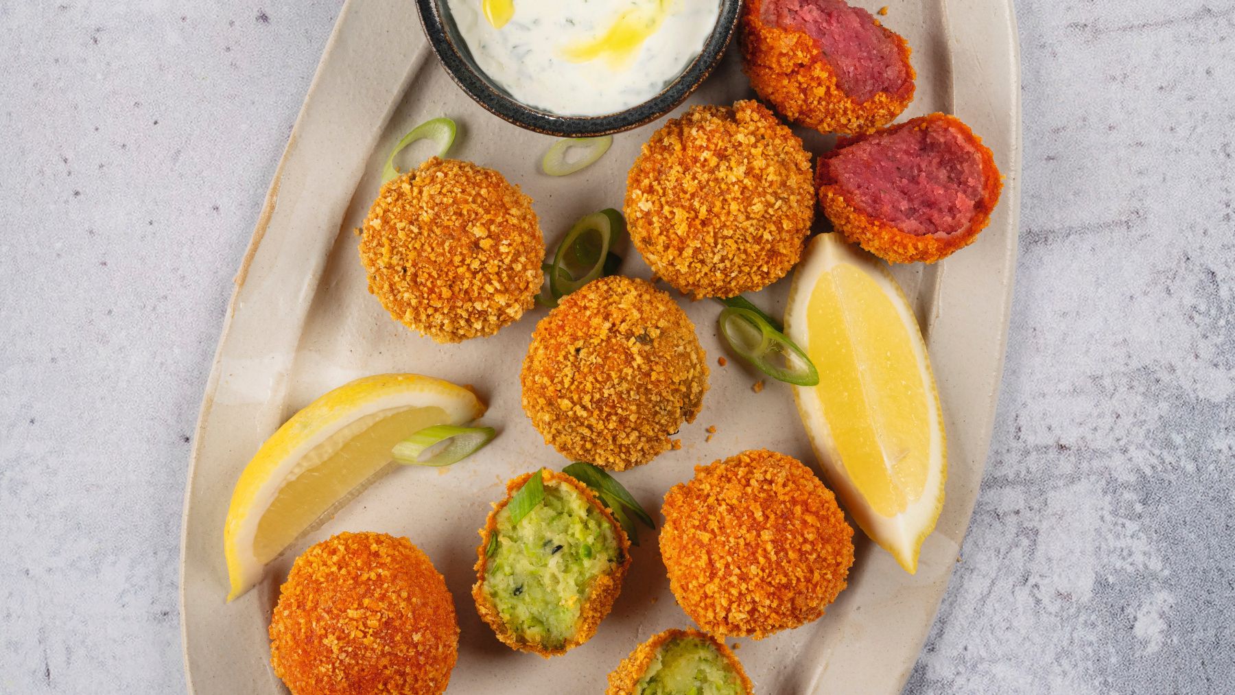 Bunte Falafel aus dem Airfryer mit hellem Dip, Zitronenspalten und frischem Gemüse auf einer ovalen Platte