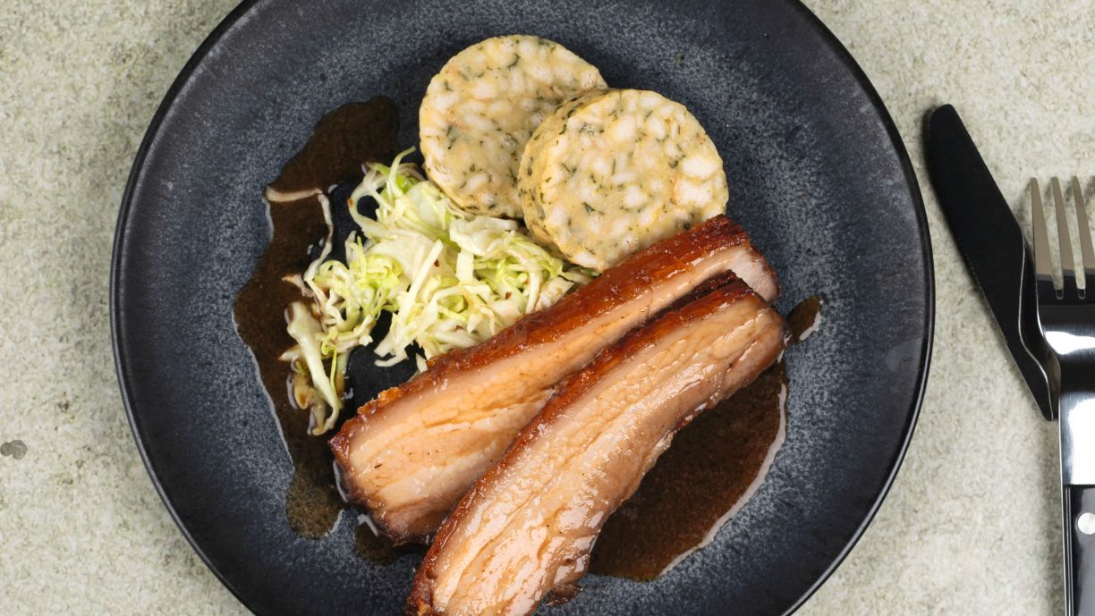 Schweinebraten im Airfryer neben einem Teller mit aufgeschnittenem Braten, Krautsalat und Beilage