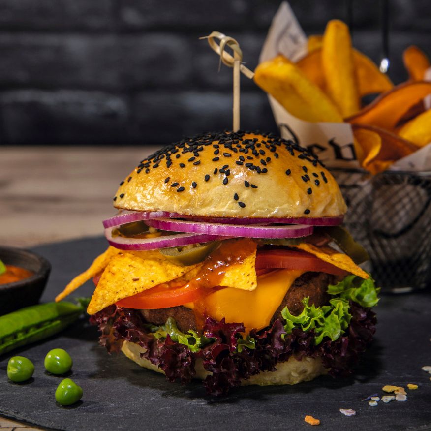 Cheeseburger mit Nachos, Salat und Tomate sowie Erbsenschote und Erbsen – Symbolbild für vegane, vegetarische und hybride Produktlösungen für Metzgereien, Lebensmittelindustrie und Systemgastronomie.