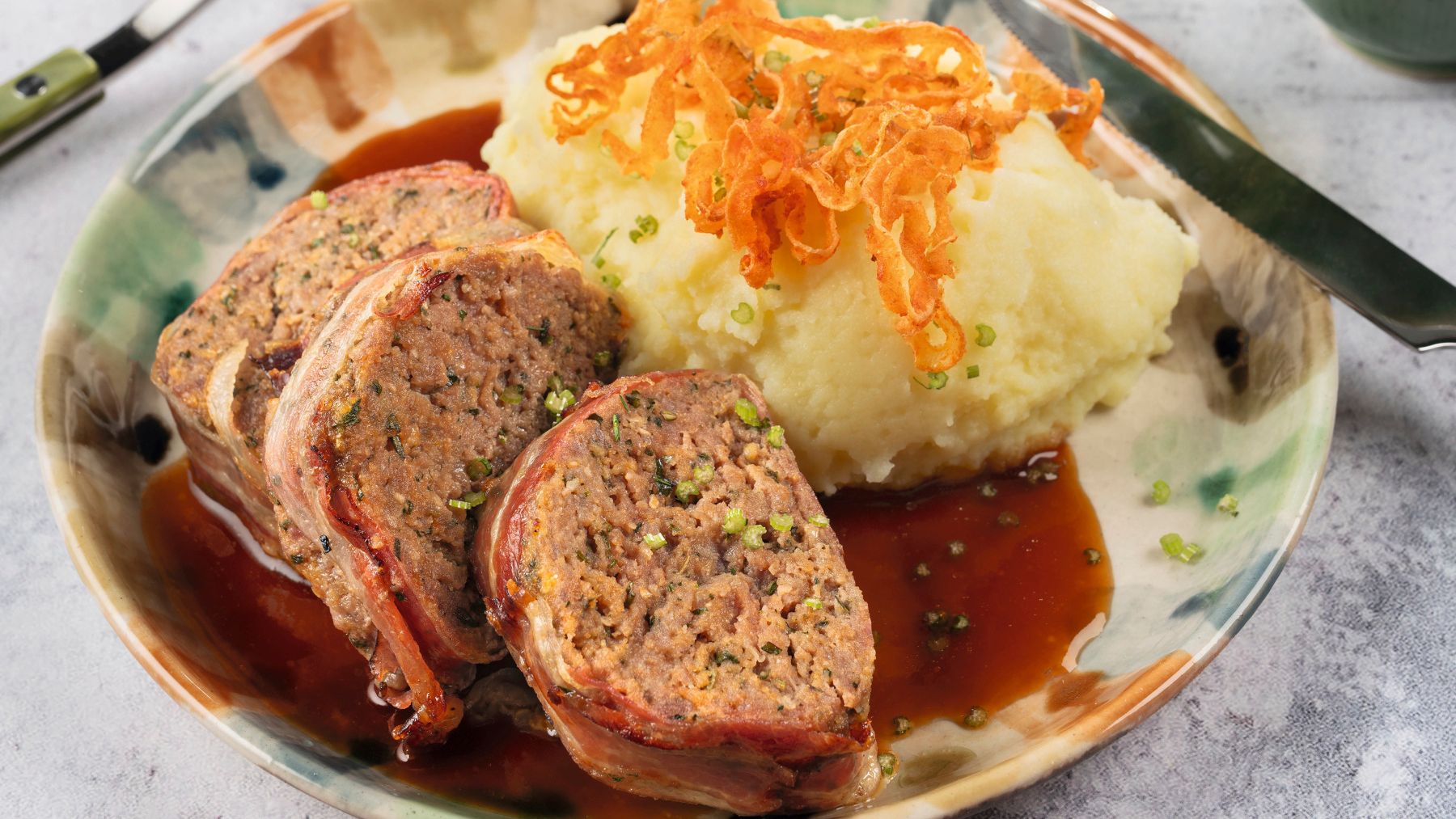Aufgeschnittener Hackbraten mit Kartoffelpüree, Röstzwiebel und dunkler Sauce auf einem Teller