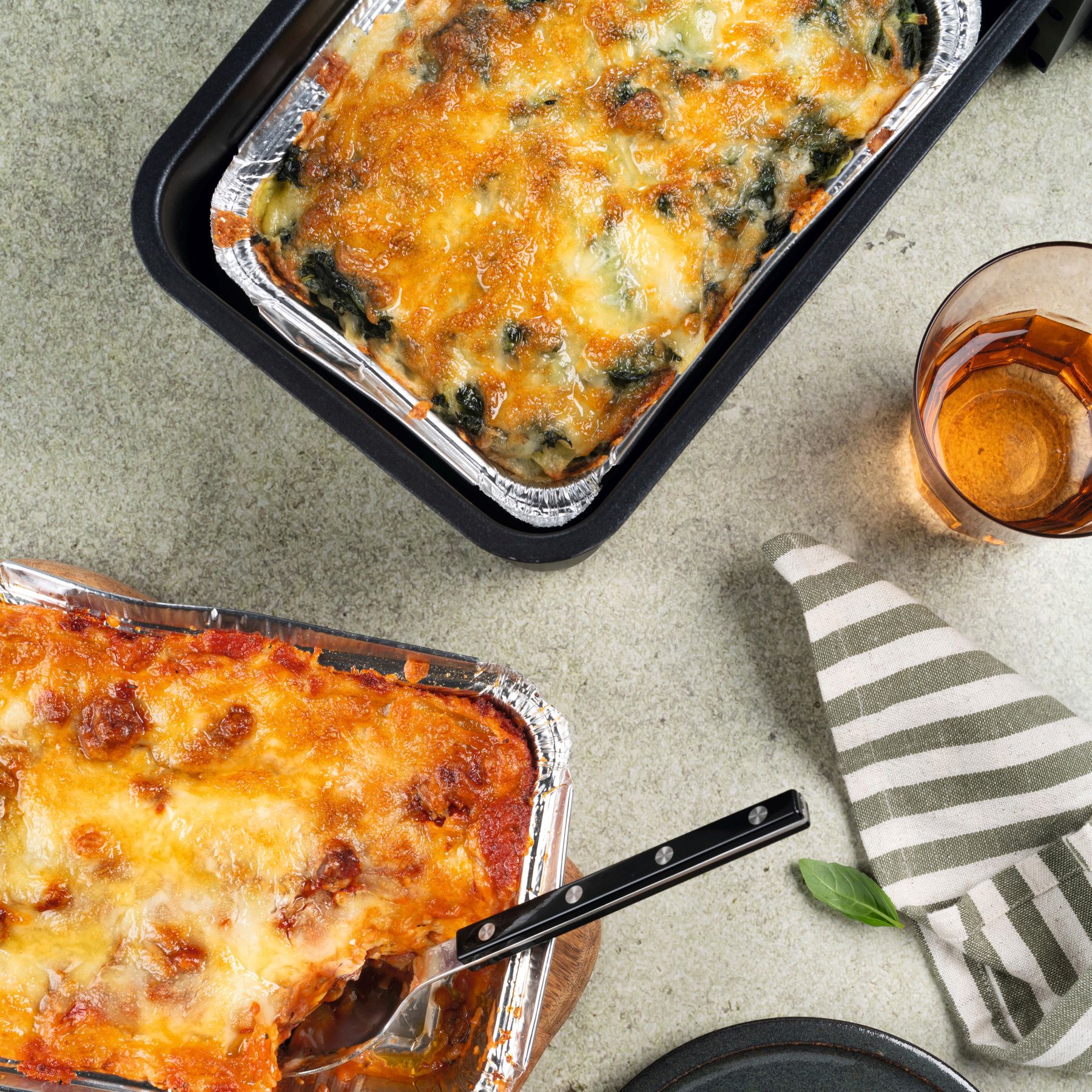Goldbraun überbackene Lasagne in zwei Auflaufformen mit einer einzelnen Portion auf einem dunklen Teller