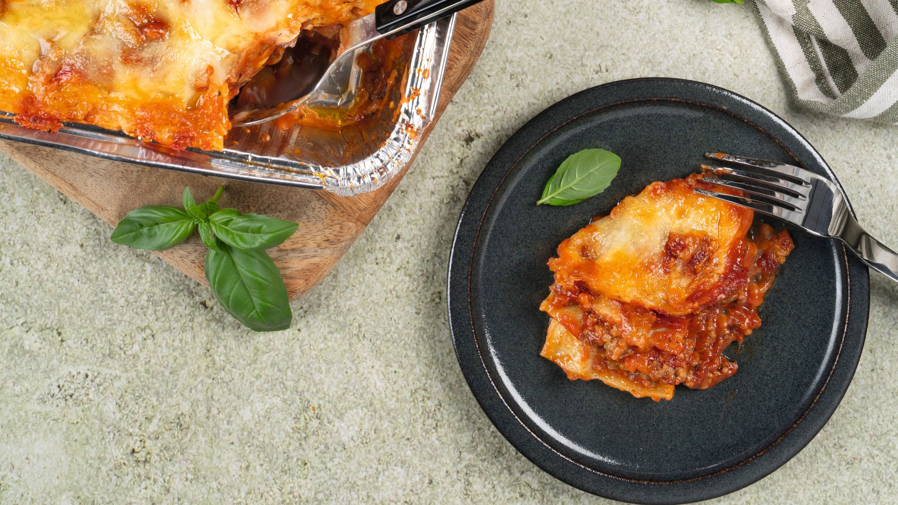 Goldbraun überbackene Lasagne in zwei Auflaufformen mit einer einzelnen Portion auf einem dunklen Teller