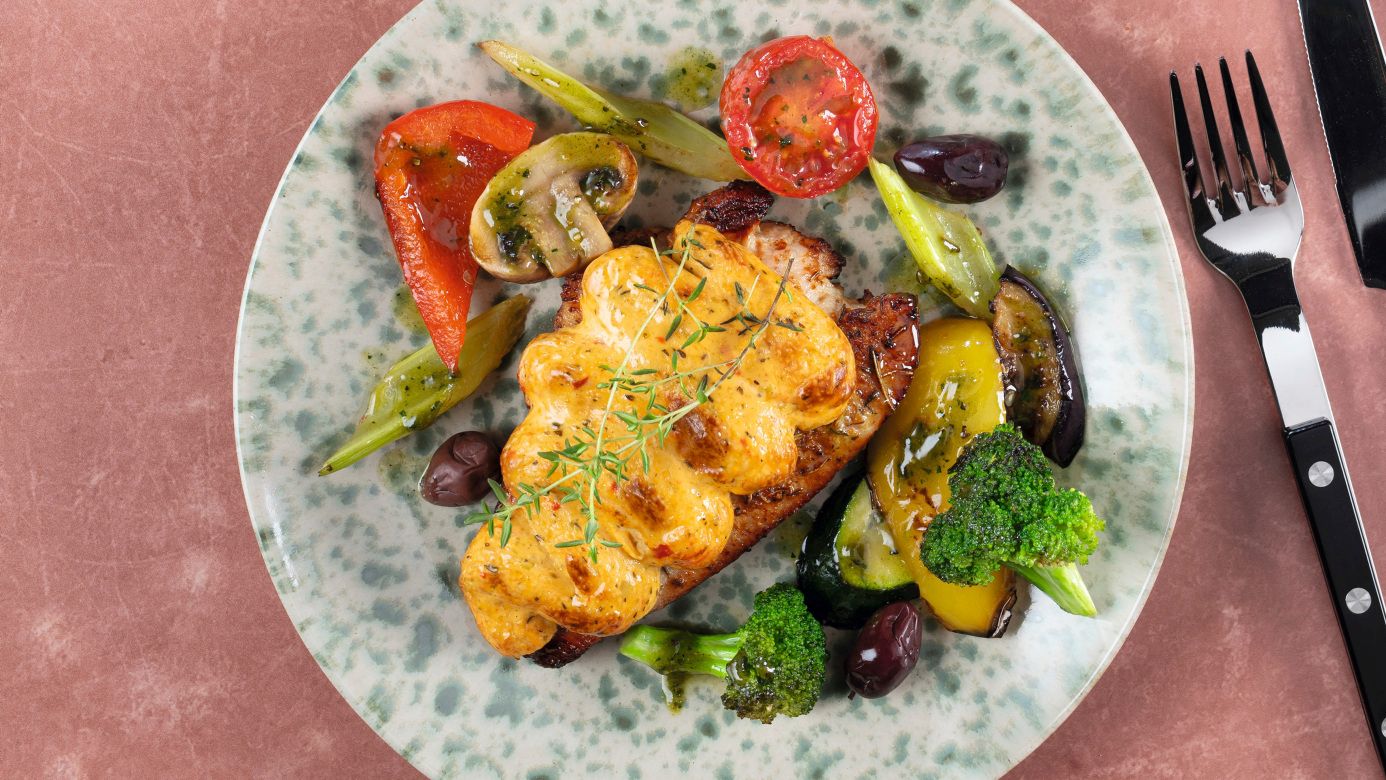 Überbackenes mediterranes Putensteak mit geschmolzenem Käse, grünem Gemüse und Tomaten auf zwei Tellern
