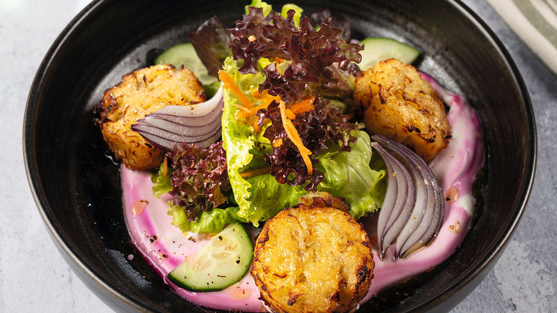 Goldbraune Rösti-Taler auf einem Salat mit Karotten, roten Zwiebeln und bunten Blattsalaten
